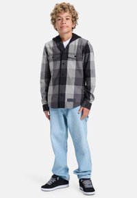 Černá a šedá kostkovaná flanelová košile s černou kapucí, dvěma kapsami na hrudi, ve spojení se světle modrými džíny a černými teniskami s bílými akcenty.