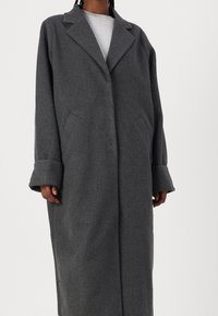 Cappotto grigio in lana con collarino a revel, maniche lunghe e tasche laterali. Presenta una vestibilità comoda e un design di lunghezza media.