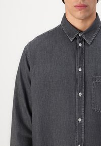 Dunkelgraues Denim-Hemd mit klassischem Kragen, langen Ärmeln und einer Brusttasche. Verfügt über eine Knopfverschluss und sichtbare Nähdetails.