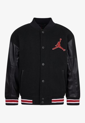 Chaqueta universitaria negra con mangas de cuero, botones a presión, puños y dobladillo a rayas, con un logo rojo de Jumpman de baloncesto en el pecho.