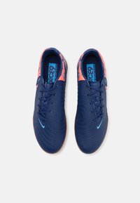 Blauwe sneakers met een gestructureerd oppervlak, voorzien van een feloranje hiel en gestipte accenten. Inclusief zwarte veters en een blauw logo.