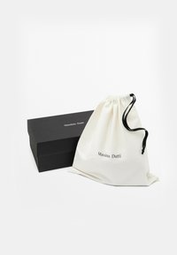 Černá obdélníková krabička Massimo Dutti vedle bílého pytlíku se černými šňůrkami, obě položeny na bílém povrchu.