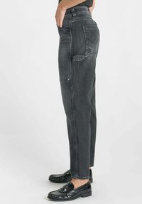 Jeans skinny taille haute en denim noir avec une coupe décontractée, dotés de poches latérales, d'une poche arrière en tissu et de détails texturés subtils.