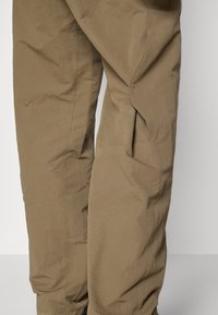 Calças caqui feitas de um tecido leve com um acabamento texturizado, apresentando bolsos laterais e costuras subtis para um detalhe adicional.