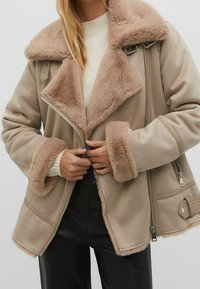Tan faux fur-lined jacket with a large collar, zip closure, and textured cuffs. Features side pockets and ribbed detailing on the hem.