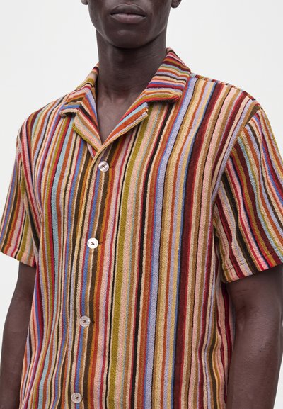 Homme portant une chemise à manches courtes boutonnée avec des rayures verticales multicolores en rouge, bleu, vert, orange et marron.