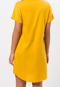 Gelbes Kurzarmkleid mit lässigem Schnitt, aus glattem Stoff gefertigt. Verfügt über umgeschlagene Ärmel und ein abgerundetes Design am Rücken.