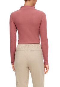 Pitkähiha toppi hillityssä ruusussa, sileä rakenne, korkea kaulus. Yhdistetty beigenvärisiin joustavavyötäröisiin housuihin, joissa on sivutaskut ja rento istuvuus.