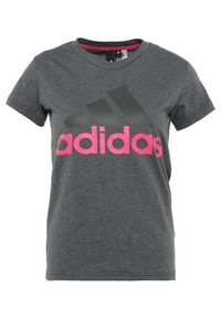 Camiseta de algodón gris con mangas cortas que presenta un gran logo rosa de "adidas" y tres rayas negras en el pecho. Escote redondo.
