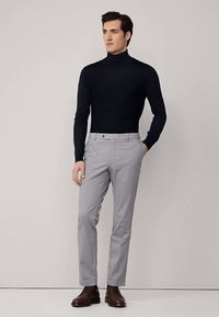 Mornarsko plavi rolka, sive krojene hlače, smeđe kožne cipele. Prilagođeni dizajn s dugim rukavima i elegantnim siluetom, minimalistički stil.