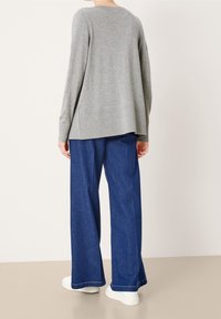 Sweater de punto gris claro con un corte relajado, escote redondeado y un detalle sutil en la parte de atrás, combinado con pantalones de mezclilla azul holgados y zapatillas blancas.