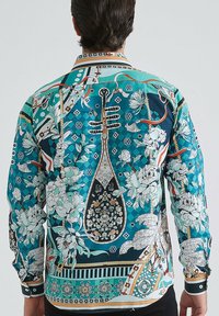 Une chemise à manches longues présente une base turquoise avec des motifs floraux et géométriques complexes, des accents contrastants et un col à boutons.