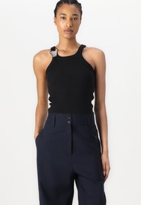 Débardeur noir à côtes avec un accent en métal unique sur l'épaule, associé à un pantalon taille haute bleu marine avec fermeture à double bouton et poches.