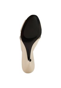 Zapato de tacón beige con un upper liso, que presenta una correa curvada y una suela negra texturizada, diseñado para ofrecer estabilidad y agarre.