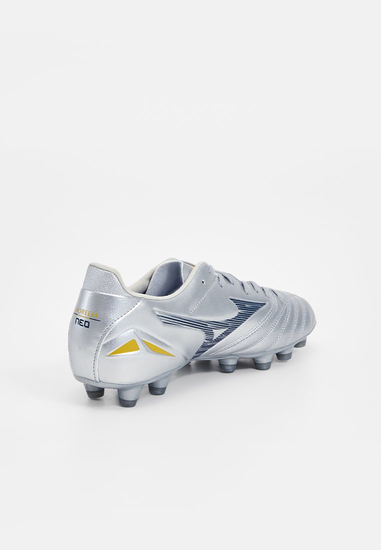 Des chaussures de football avec un dessus en synthétique argenté, des rayures texturées et des accents bleu marine, dotées de pièces jaunes et d'une semelle moulée pour l'adhérence.