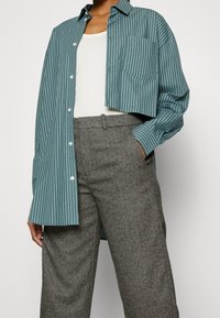Groene en witte gestreepte cropped button-up shirt, gecombineerd met grijze textuurbroek, voorzien van een zijzak en een relaxte pasvorm.