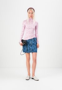 Top a maniche lunghe, di colore rosa con motivo floreale, abbinato a una gonna in denim blu con una stampa sottile. Scarpe bianche slip-on e una borsa nera.