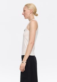 Heled beez tank top, mis on keha järgi sobiv ja valmistatud pehmest kangast. Omab ümarat kaelust ja minimalistlikku esteetikat. Kombineeritud tumedate pükstega.