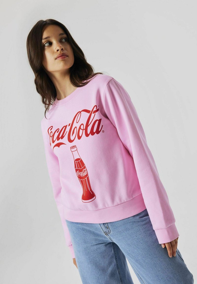 Felpa rosa con il logo e la grafica di una bottiglia rossa della Coca-Cola. Maniche lunghe, scollatura tonda e polsini e orlo a costine. Tessuto testurizzato.