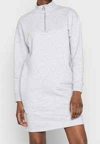 Grå sweatshirtklänning i mjukt tyg, med hög krage, långa ärmar och dragkedjeslutning vid halsen. Enkel design.