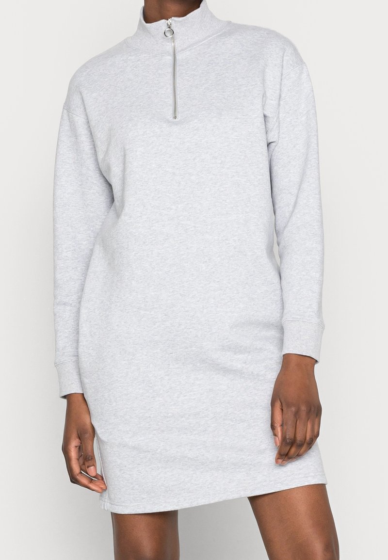 Grå sweatshirtklänning i mjukt tyg, med hög krage, långa ärmar och dragkedjeslutning vid halsen. Enkel design.