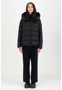Schwarze Daunenjacke mit großer Kapuze, gestepptem Design und zwei Reißverschlusstaschen vorne. Getragen mit schwarzen weit geschnittenen Hosen und Plateau-Schuhen.