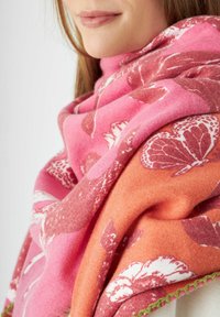 Écharpe rose et orange à motifs floraux, avec une texture douce et une bordure verte texturée sur le bord.
