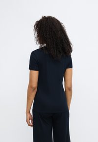 Zwart topje met korte mouwen gemaakt van een gladde, lichtgewicht stof. Getailleerd ontwerp met een ronde halslijn en subtiele stiksel details aan de achterkant.