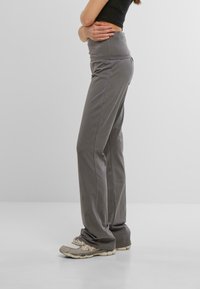 Pantaloni attivi grigi con vita alta, design a gamba dritta e texture morbida. Abbinati a scarpe da ginnastica chiare.