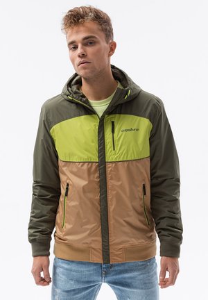 Grøn og beige hættejakke med lynlås foran, kontrasterende paneler, sidelommer og "ombre" logo på brystet. Tekstureret, letvægtsmateriale.