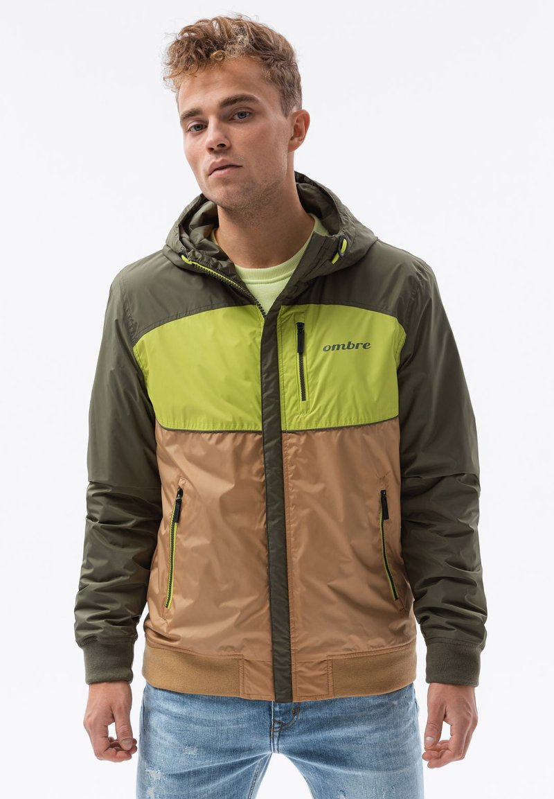 Grön och beige huva jacka med dragkedja fram, kontrasterande paneler, sidofickor och "ombre" logotyp på bröstet. Texturerat, lätt material.