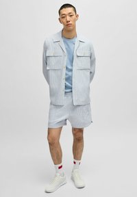 Lichtblauw gestreept overhemd met korte mouwen en twee borstzakken, gecombineerd met bijpassende shorts en witte sneakers, met sokken met rode accenten.