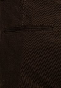 Tissu en velours côtelé marron présentant des côtes verticales et une poche arrière unique avec un détail de couture horizontale.