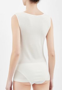 Top senza maniche di colore crema, con una texture liscia, collo rotondo e una forma leggermente aderente, progettato per il comfort.