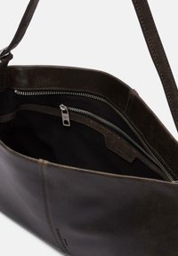 Ciemnobrązowa skórzana torba na ramię z srebrnym zamkiem błyskawicznym i czarną materiałową podszewką wewnętrzną, częściowo otwarta, ukazująca wewnętrzną kieszeń na zamek.