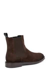 Botas de ante marrón hasta el tobillo con paneles laterales elásticos y una tira de sujeción. Textura suave con punta redonda y suela plana de goma.
