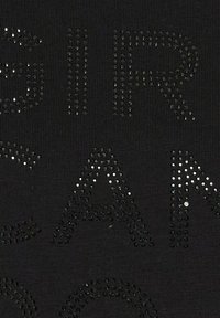 Sort stof med forhøjede rhinstenbogstaver i et mønster, der staver 'GRL PWR' med forskellige størrelser og placeringer af stenene.