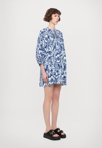 Blauwe jurk met bloemenprint, met een losse pasvorm, poffende mouwen en een keyhole-halslijn. G gedragen met zwarte plateausandalen met gesps details.