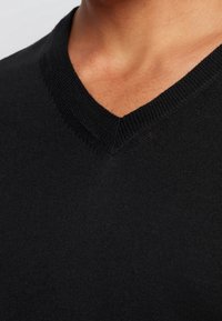 Černý pletený svetr s V-výstřihem a žebrovaným límcem. Materiál je hladký a lehký, vykazuje texturu blízko pokožky.