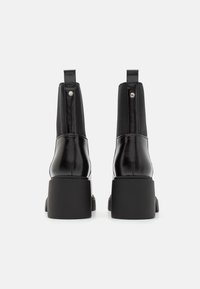 Svarta ankelstövlar med blankt läderöverstycke, elastiska sidor och en klumpig matt svart klack. Bakre ögla för enkel påtagning.