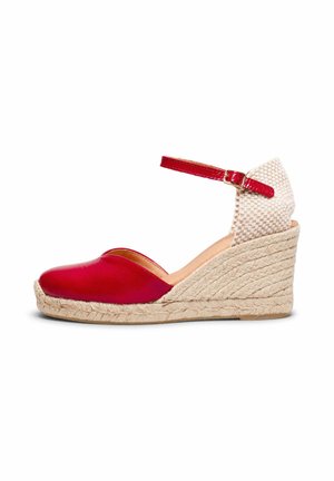 Alpargata de cuña cerrada roja con tacón tejido beige y hebilla en la correa del tobillo sobre fondo blanco.