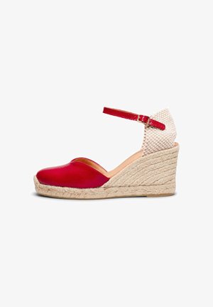 Alpargata de cuña cerrada roja con tacón tejido beige y hebilla en la correa del tobillo sobre fondo blanco.
