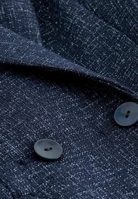 Tela texturizada de color azul marino con un patrón tejido, dos botones negros visibles, con un ligero brillo y un detalle textil intrincado.