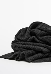 Écharpe noire en tricot avec un tissu doux et texturé ; elle présente un motif côtelé, drapée légèrement, créant des plis et des couches délicates.