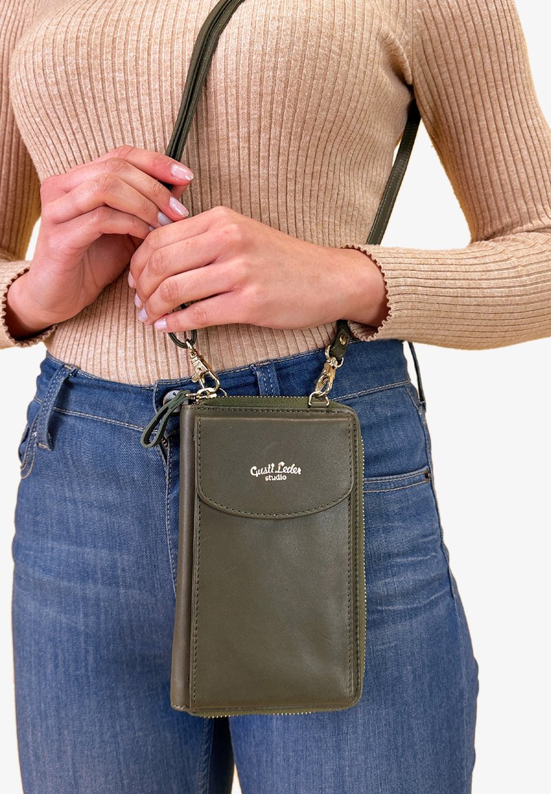 Olivengrøn læder crossover taske med frontklap, lynlåslukning og hardware i guldtone. Teksturfinish, kompakt design og justerbar rem.