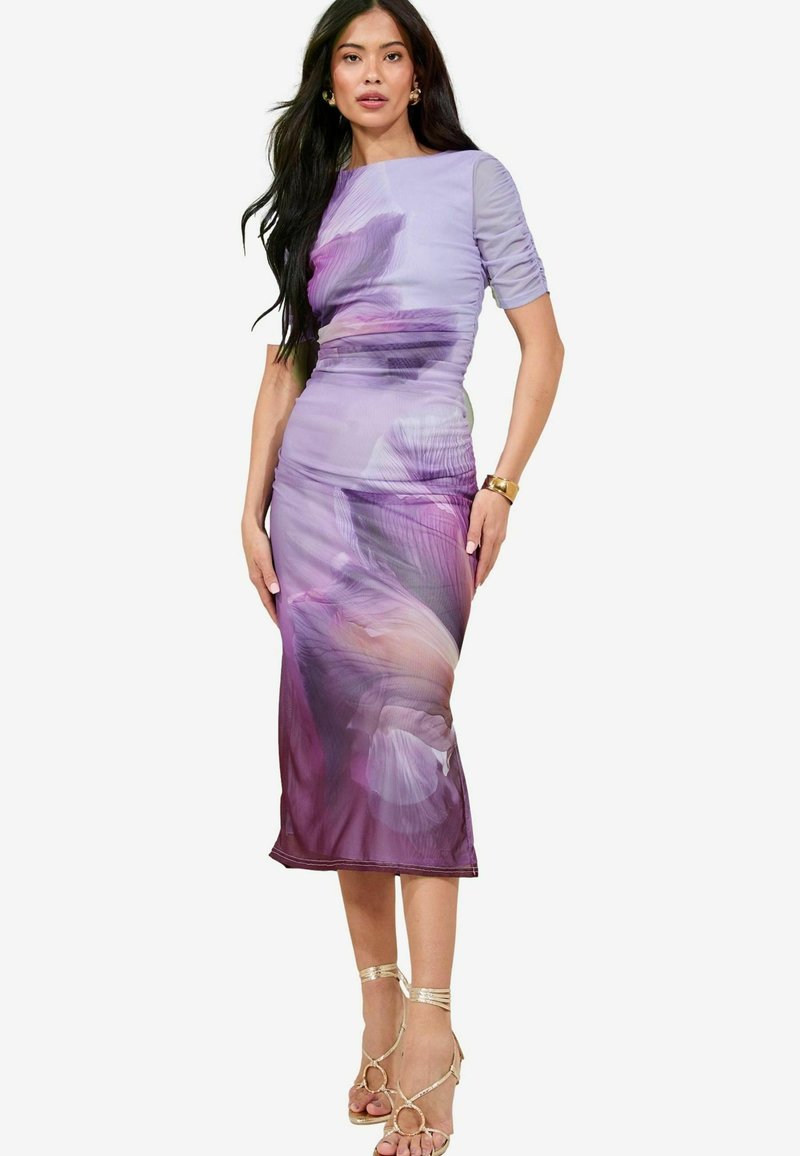 Lila kukallinen midi-mekko, jossa on istuva siluetti, rypytystä hihoissa ja läpinäkyvää kangasta. Yhdistetty -kultaisiin, remmillisiin sandaaleihin.