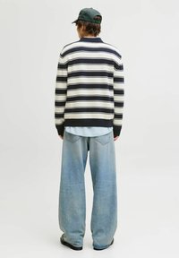 Pruhovaný svetr v námořnické modři a krémové barvě, spárovaný s světle modrými širokými džíny. Model má na sobě tmavě zelenou kšiltovku a náušnici, viděno zezadu.