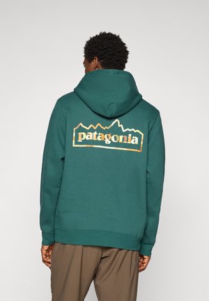 Turquoise hoodie featuring a large white and orange "patagonia" logo with mountain peaks design on the back; soft fabric, drawstring hood.