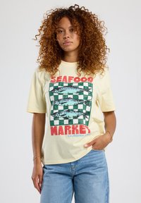 Light yellow cotton t-shirt featuring a graphic design with fish, green and white checkered pattern, and red text reading "SEAFOOD MARKET."