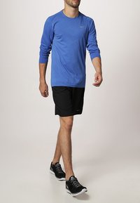 Niebieska koszulka sportowa z długim rękawem i teksturowanym wzorem, zestawiona z czarnymi szortami i czarnymi butami do biegania, przedstawiająca swobodny sportowy look.